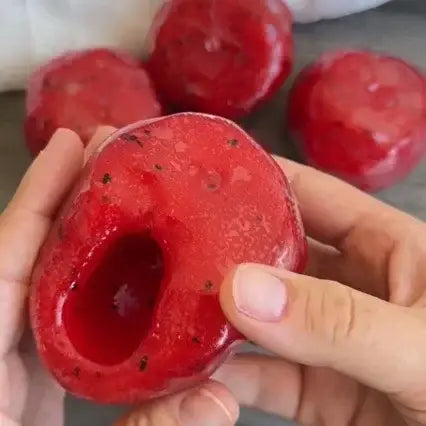 A translucent red glossy faceted resin apple-shaped watermelon slushy squishy stress relief toy with a hollow center and embedded black specks.