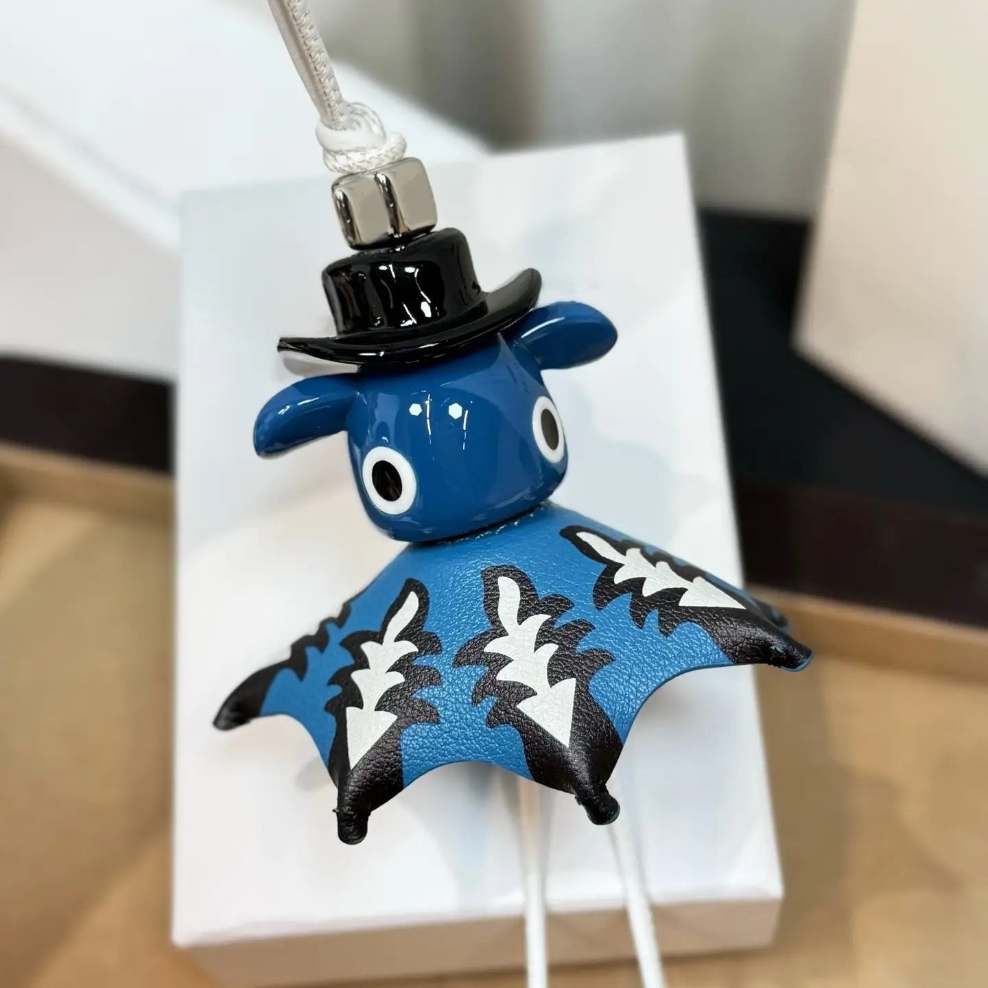 Llavero colgante para bolso con encanto de animales de cuero, tierno, de diseñador, con un llavero de cuero con forma de murciélago azul, alas con patrón en blanco y negro, usando un bombín superior negro brillante.