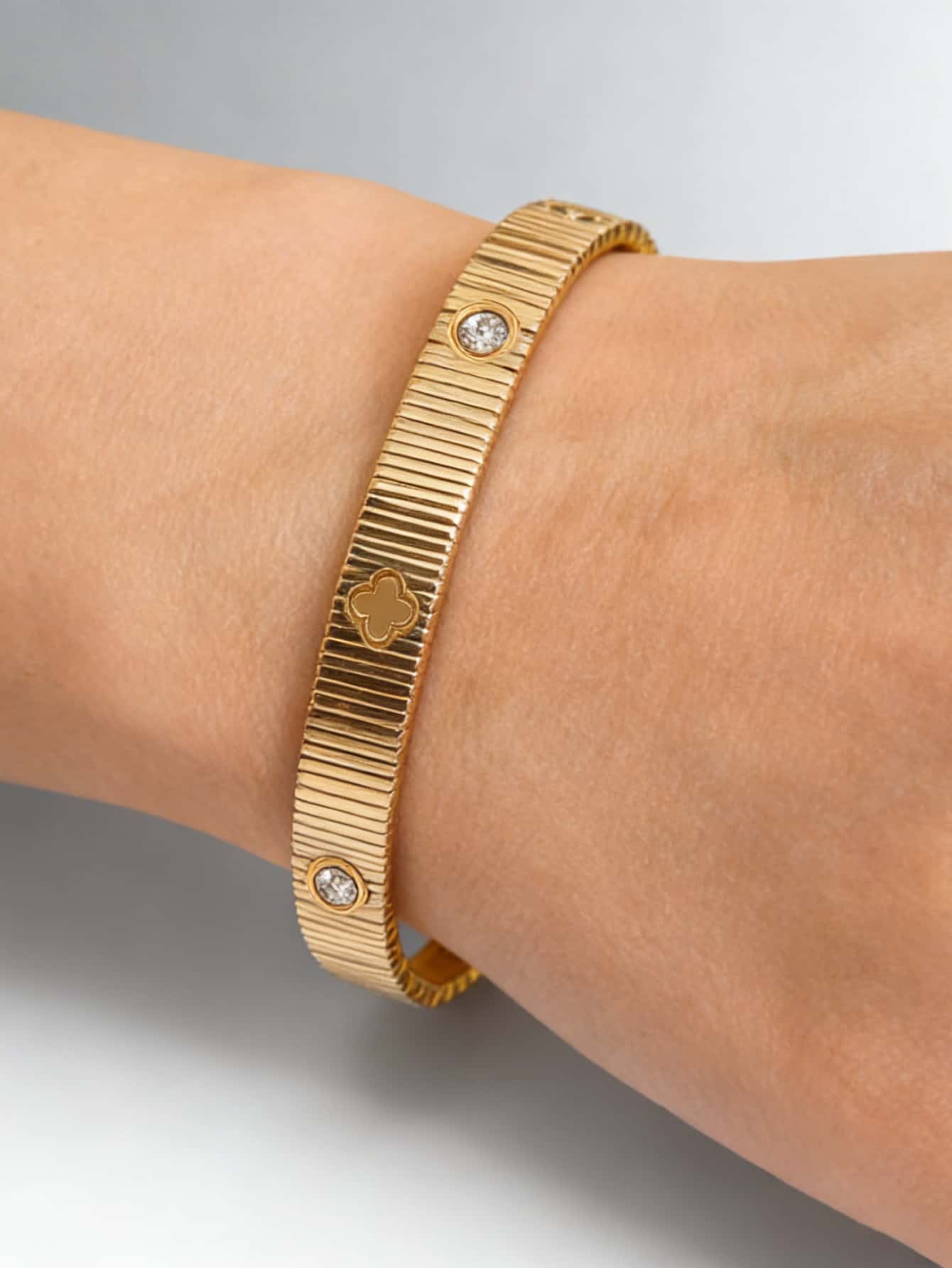 Pulsera tipo brazalete con cruz de cristal con acabado dorado, diseño acanalado con motivo de trébol y dos acentos de diamante redondos.