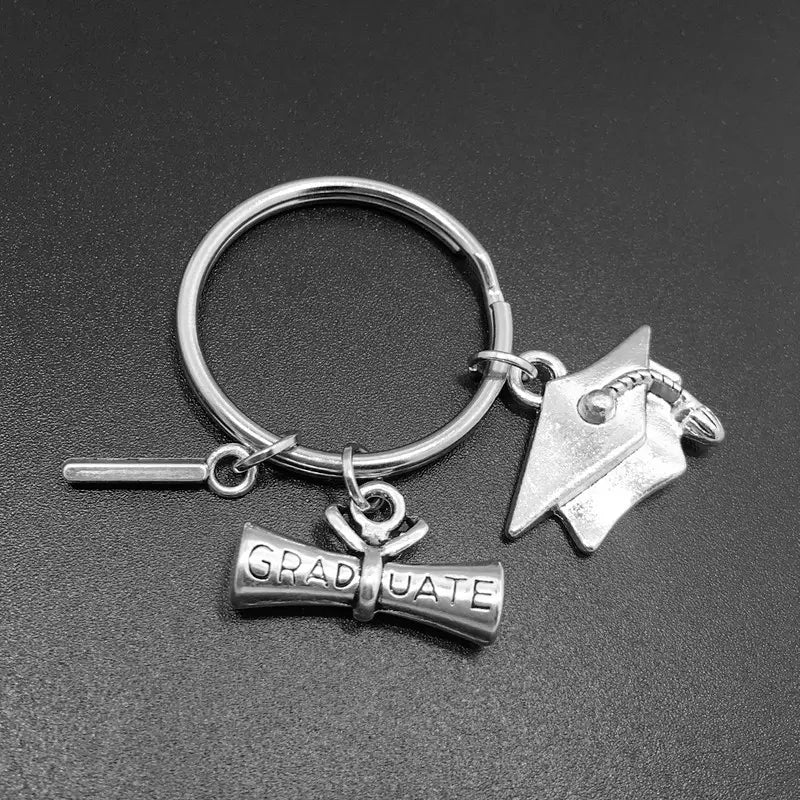Silberner Schlüsselanhänger zur Abschlussfeier mit einer Abiturmütze, einem mit Graduate gravierten Diplom-Anhänger und einem Stift-Anhänger zur Erinnerung an den akademischen Erfolg.