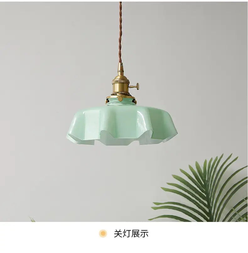 Un luminaire suspendu délicat à jupe florale en verre vert menthe avec une conception cannelée en forme de pétales et une tête de lampe en cuivre montrée depuis l’avant.
