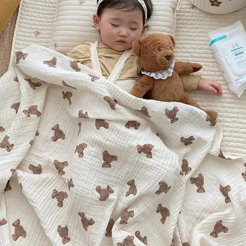 ein weiches Baby-Badehandtuch und eine Wickeldecke aus Muslin in einem sanften Off-White mit einem wiederholenden Muster kleiner brauner Teddybären