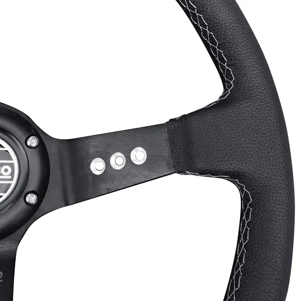 El volante de carreras universal de 14 pulgadas en PVC negro presenta una envoltura de cuero negro con costuras de contraste blancas y un cubo central metálico negro.