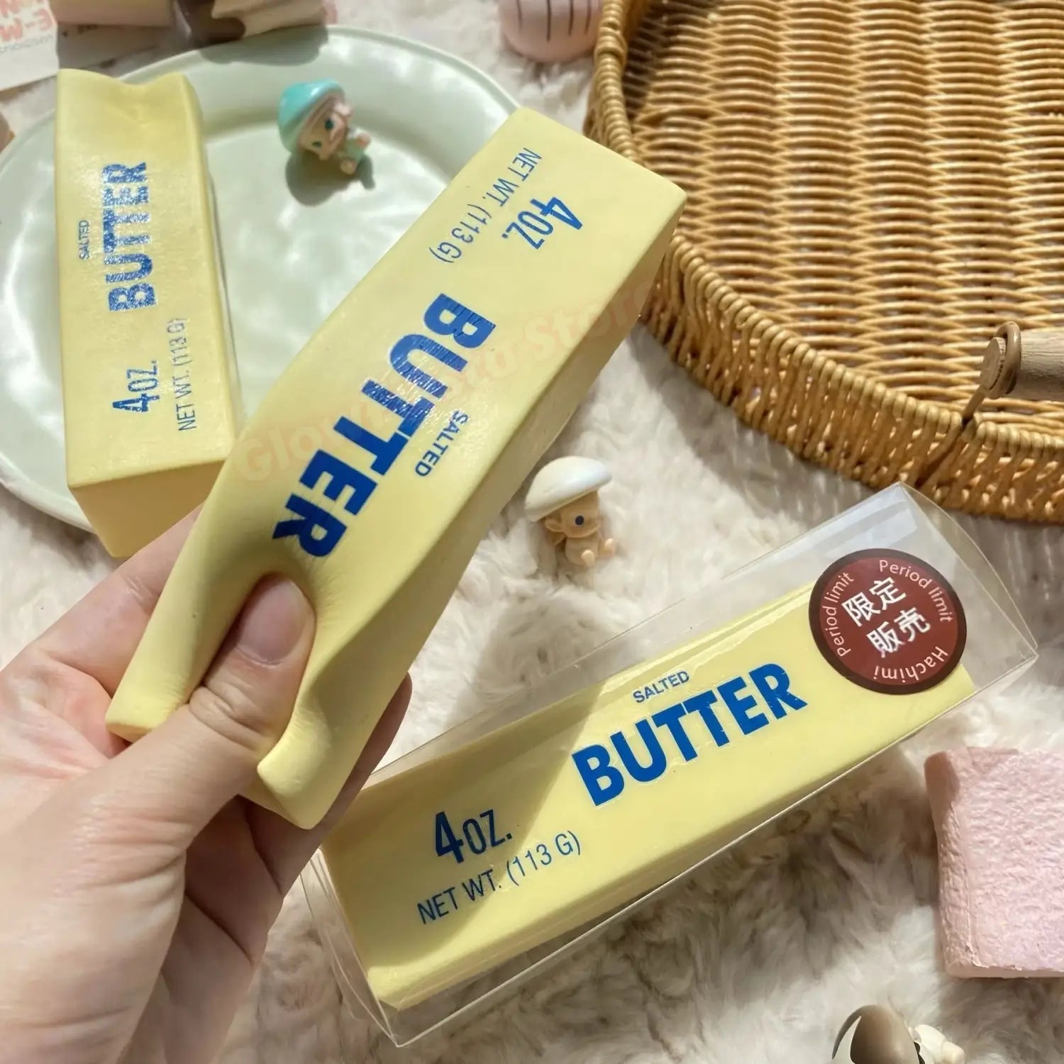 Un bâton de beurre salé jaune avec lettrage bleu, dans un récipient en plastique transparent, conçu comme un jouet antistress à montée lente, en assortiment de 12.