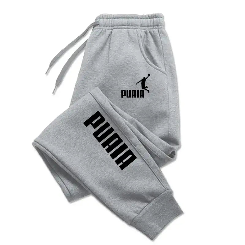 Joggers impresos de hombre estilo casual streetwear de Puma en color gris, con logotipo y letras en color negro.