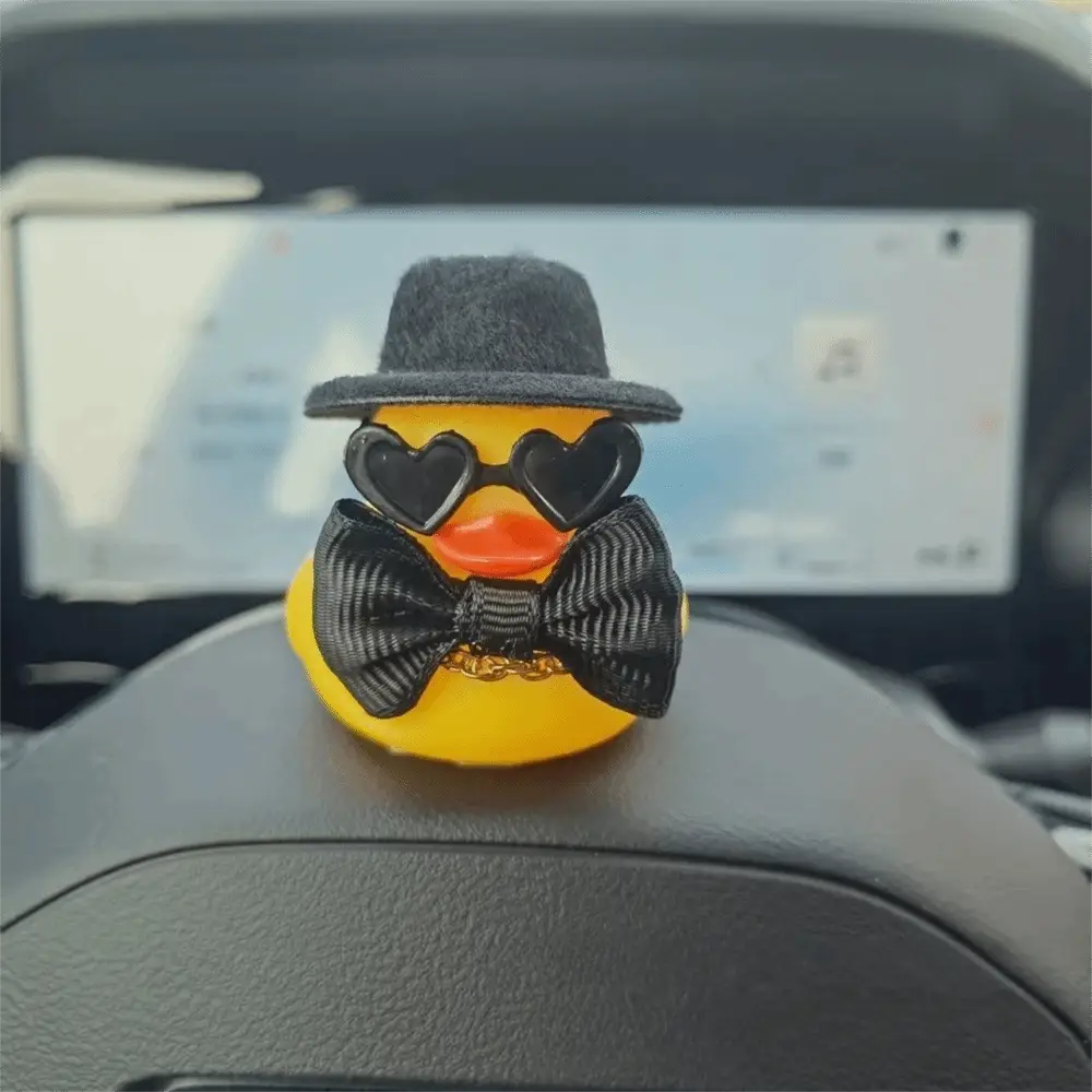 adorno de boda de patito de goma amarillo que lleva un fedora negro, gafas con forma de corazón y una pajarita negra con detalles de cadena dorada.