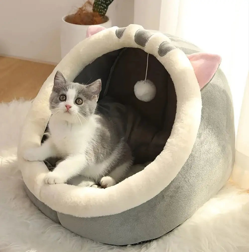 Plüsch-Cat-Cave-Bett aus weichem grauem und weißem Plüschmaterial mit rosa Ohren und einem hängenden Pomponspielzeug im Inneren, ausgelegt als waschbare Haustier-Schlafmatte.