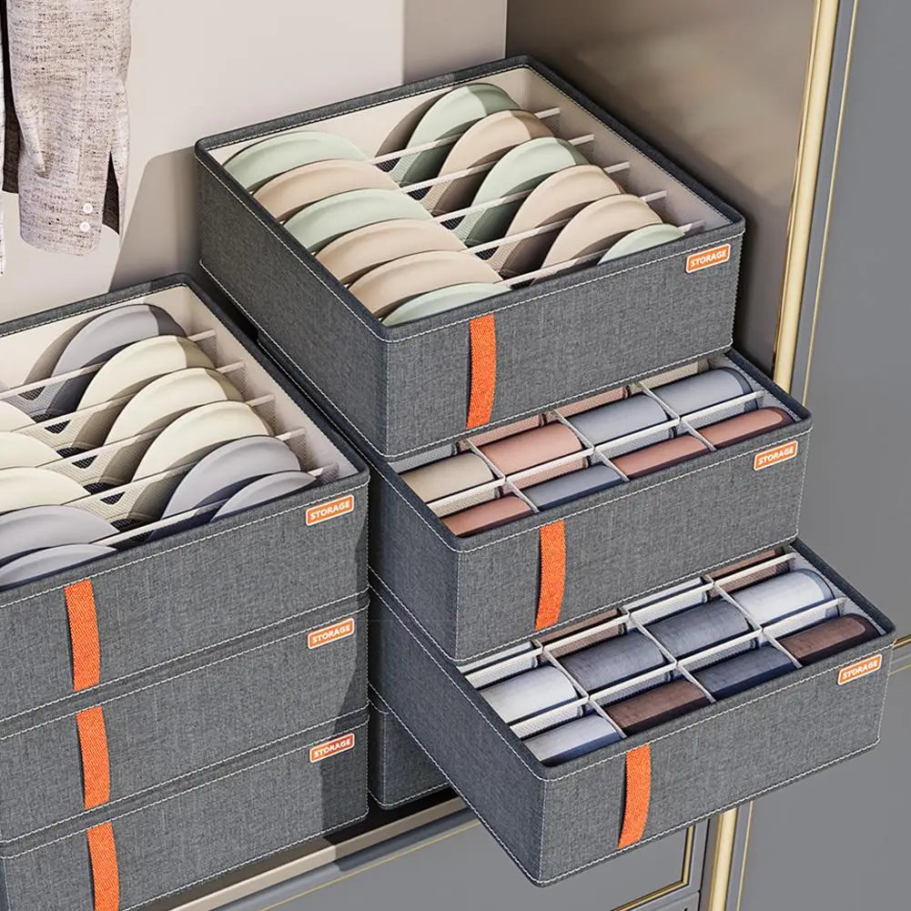 Graue Stoff-Schubladenorganizer-Box für Unterwäsche und Socken mit orangefarbenen Reißverschluss-Ziehern und Aufbewahrungsschildern, ausgelegt zum ordentlichen Aufbewahren von BHs oder Unterwäsche.