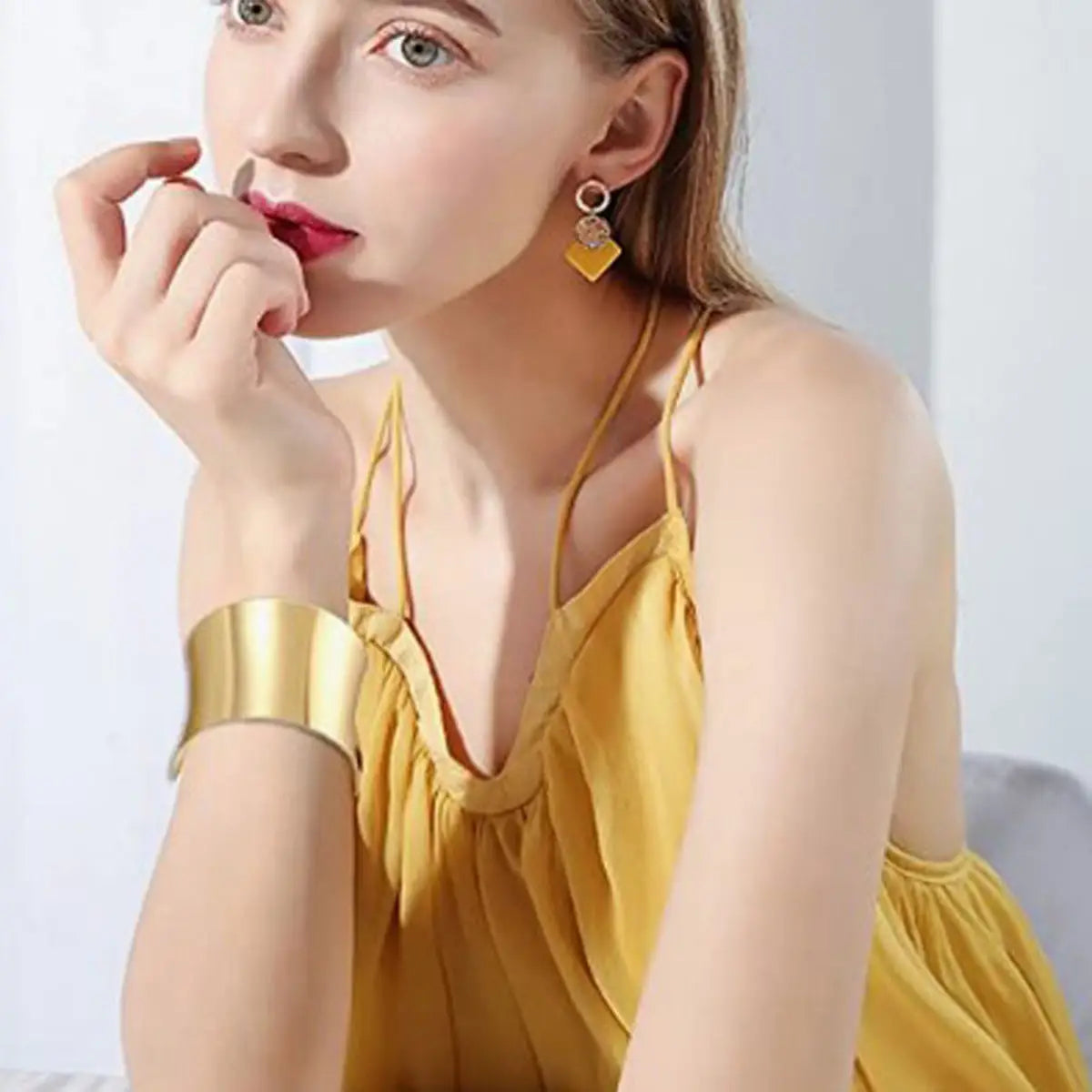 Bracelet manchette en fil plaqué or présentant un design large ton sur ton, avec une finition métallique polie et épurée.