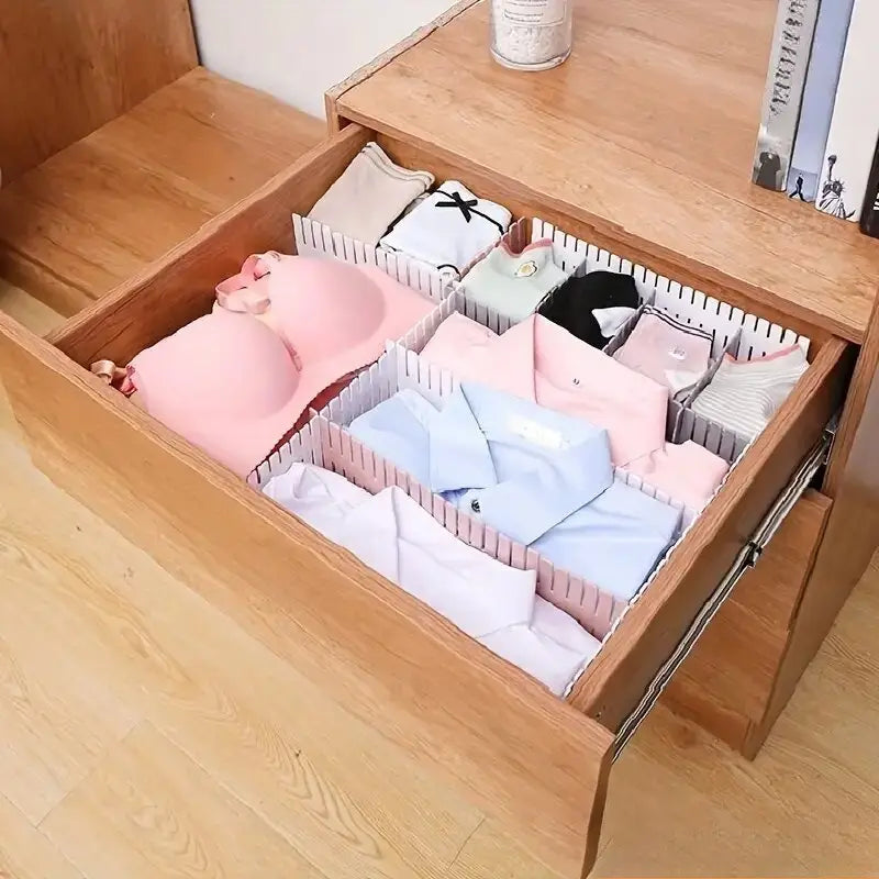 Adjustable white plastic drawer divider partition with pink flexible dividers organizing neatly folded clothing items.