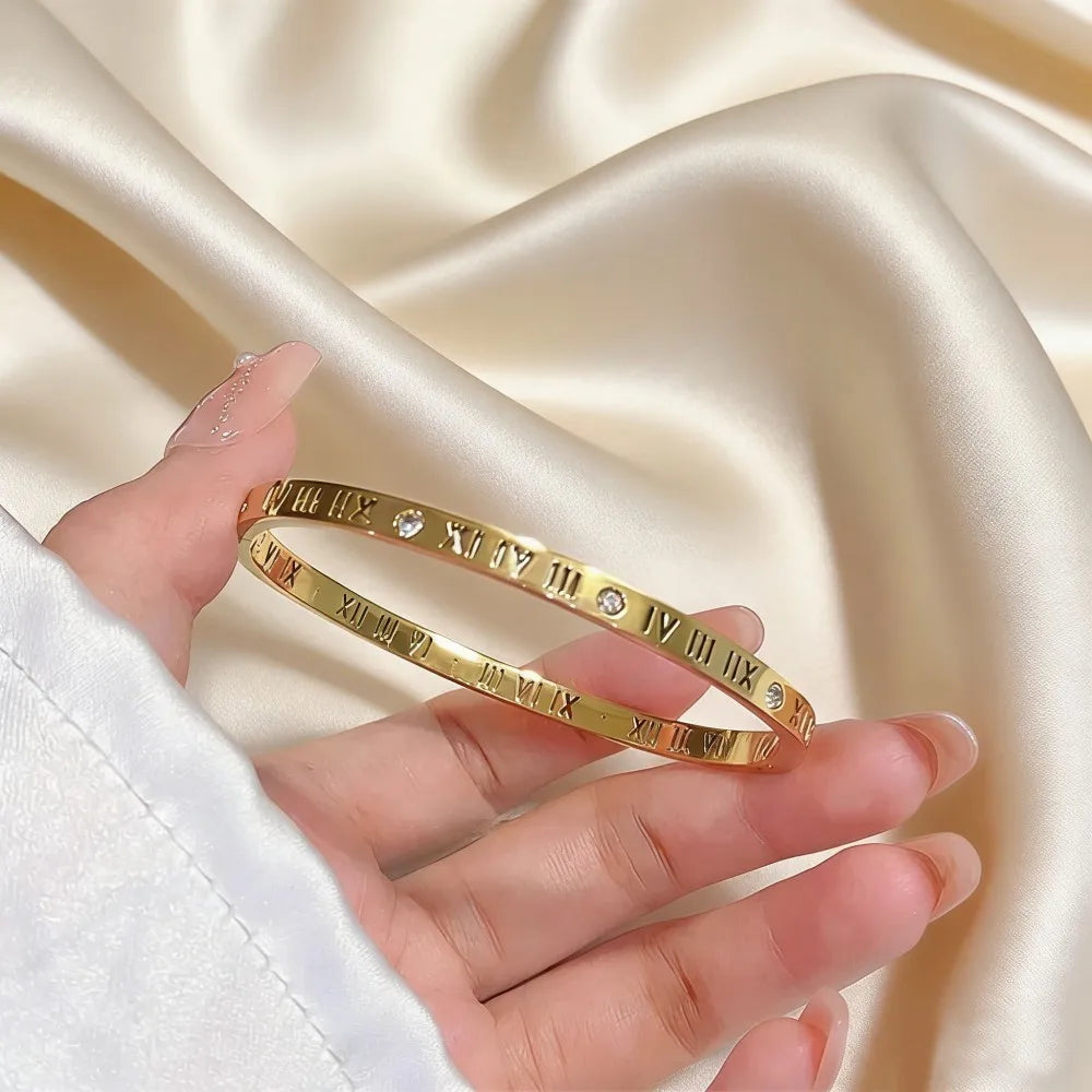 Stainless steel gold-toned bangle bracelet for women featuring engraved roman numerals and small embedded diamonds.