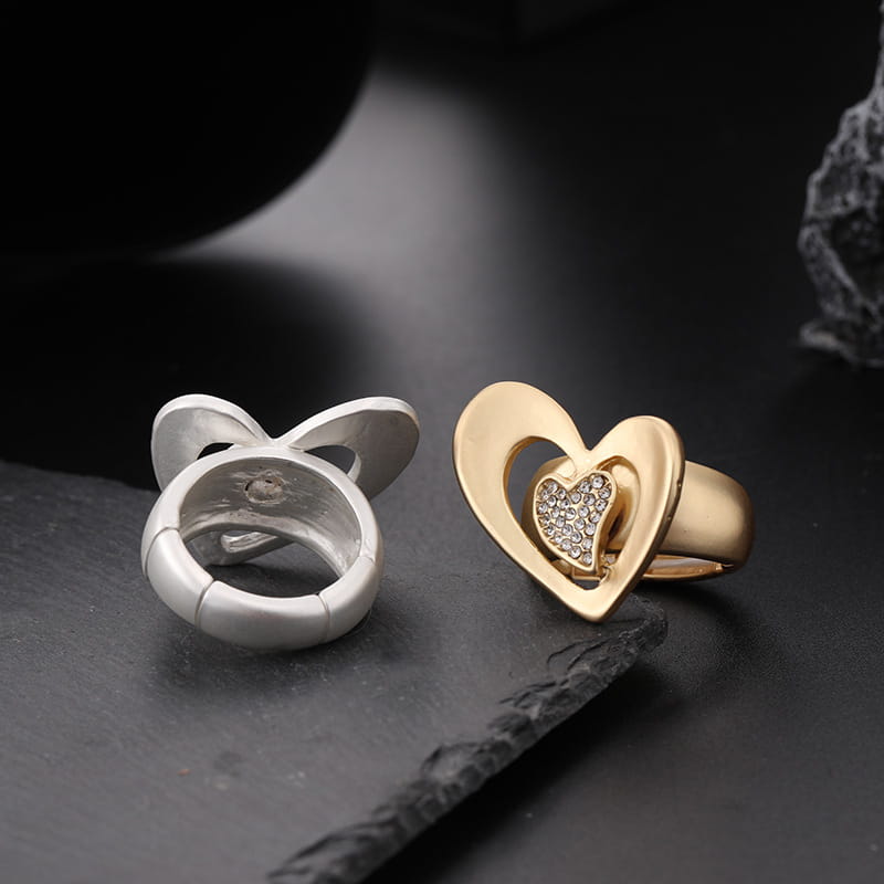 Anillo de corazón en tono dorado con pedrería tipo pavé, combinado con un anillo abstracto de eslabón abierto en tono plateado con diseño de joyería ajustable.