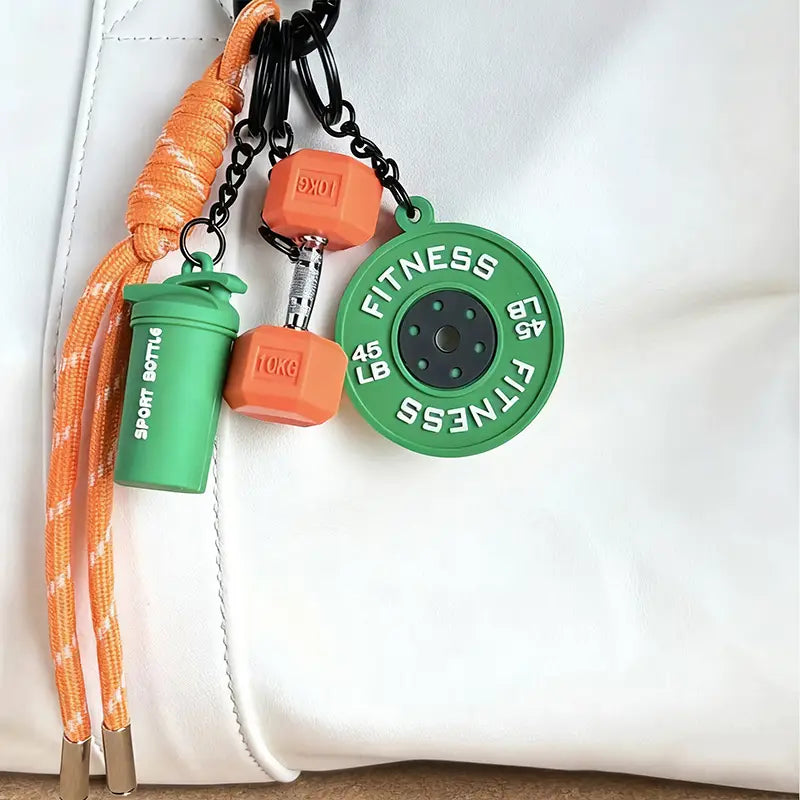 Un porte-clés de fitness orange et vert avec des breloques d’haltère en caoutchouc, de disque de poids et de bouteille shaker pour les accessoires de sac de sport.