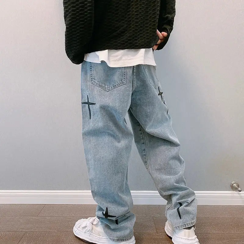 Face arrière d’un pantalon cargo en jean à jambes larges à effet délavé clair, avec broderie croisée noire sur les poches arrière et les poignets.