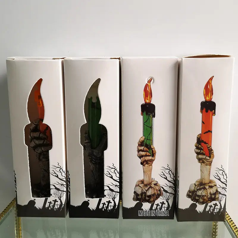 four halloween-themed led skeleton hand candles with glowing orange and green flames and black wax drips in decorative boxes for party happy halloween and happy halloween party.