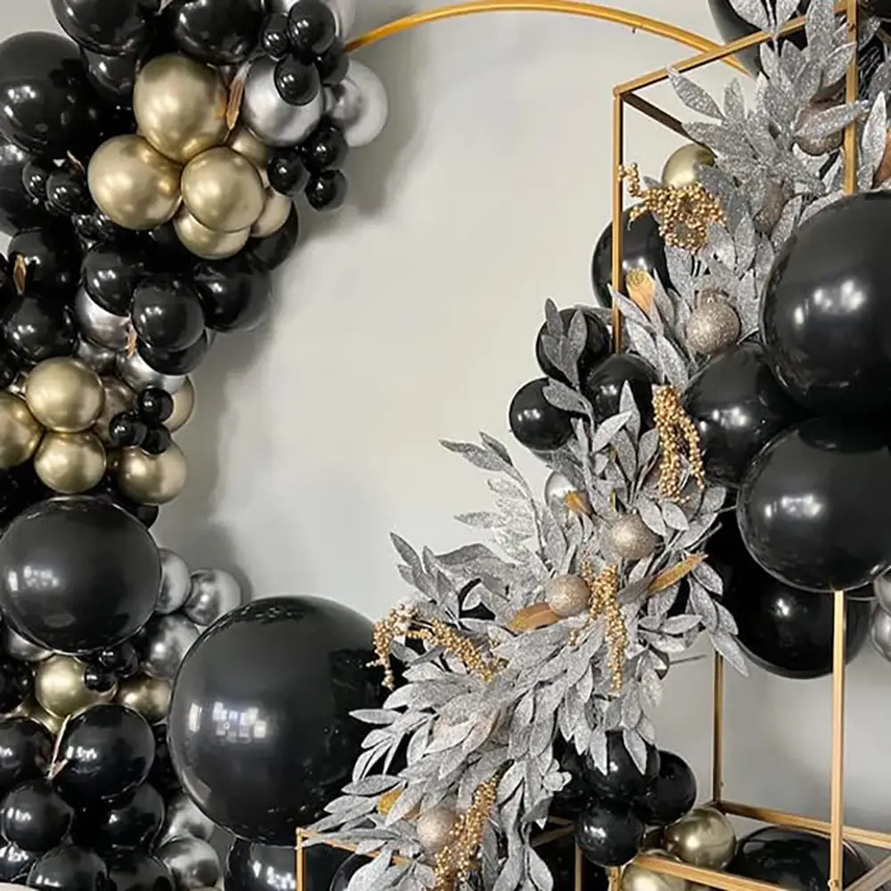 Schwarzes und goldenes Ballonbogen-Set mit schwarzen, goldenen und silbernen Ballons, verziert mit glitzerndem Grünzeug, für die Dekoration einer Party.