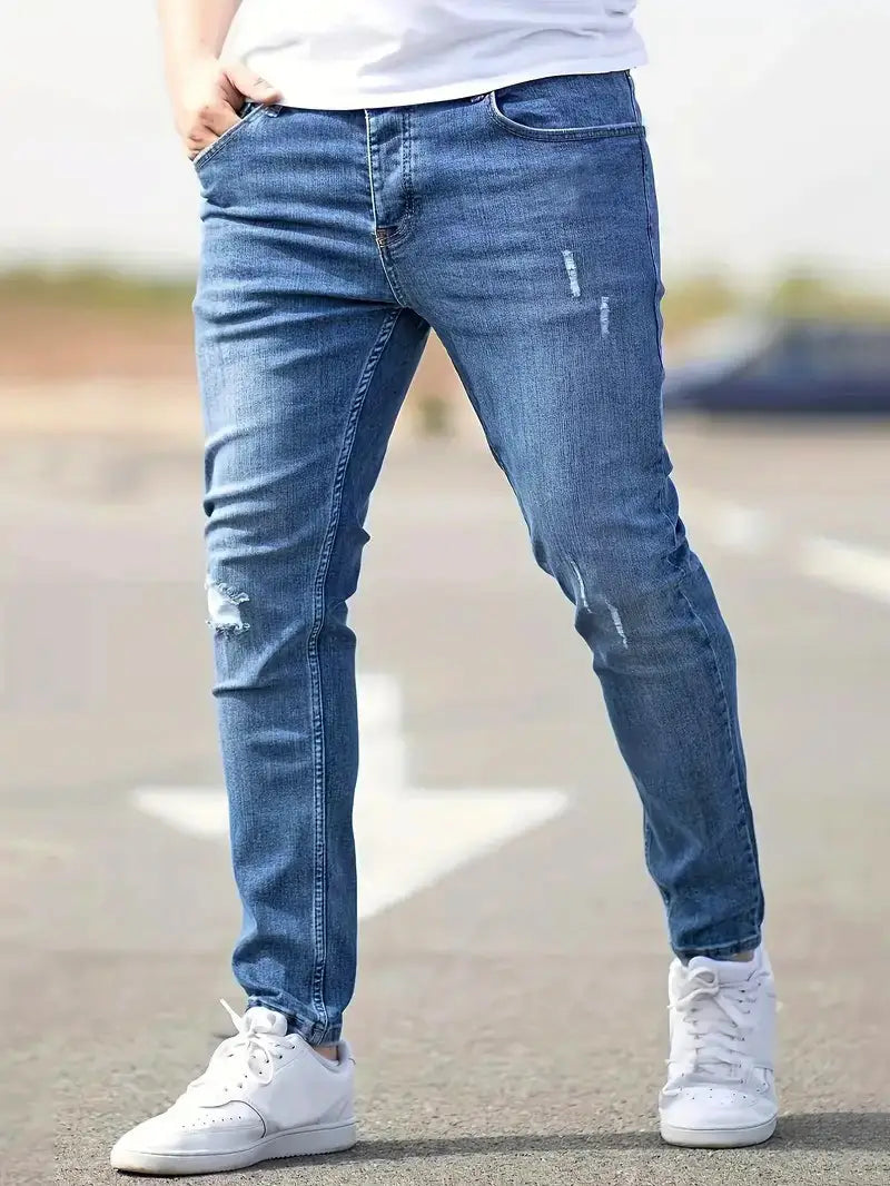 Men distressed skinny jeans in blue denim with ripped details on the knees and thighs showcasing a vintage slim fit design.