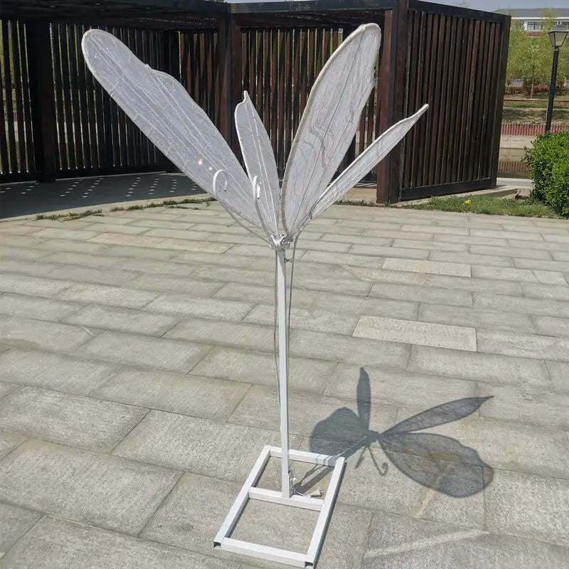 Weiße Metall-Feenflügel-Skulptur mit durchscheinenden, aderigen Flügeln und schlankem Stiel, montiert auf einer quadratischen Basis, dargestellt in der leuchtenden, an der Decke hängenden Hochzeitstennenlichtanlage mit Schmetterlingsflügeln.