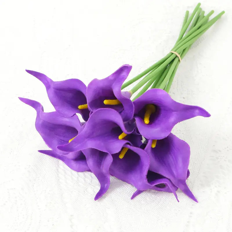 a bundle of artificial purple calla lily flower bouquet with yellow centers and green stems tied together for home decor