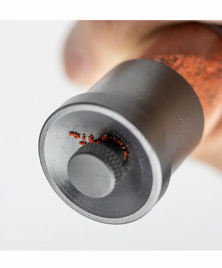 black metal feeder mini pepper mill with textured knob and fine-ground red peppercorns spilling from the opening designed as aquarium accessories small fish food dispenser