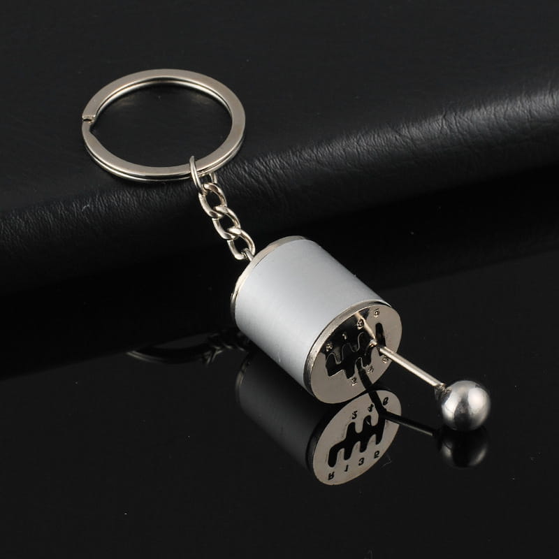 Silver metallic manual gear shift car keychain made of metal with a polished finish and engraved gear pattern on the cylindrical body.