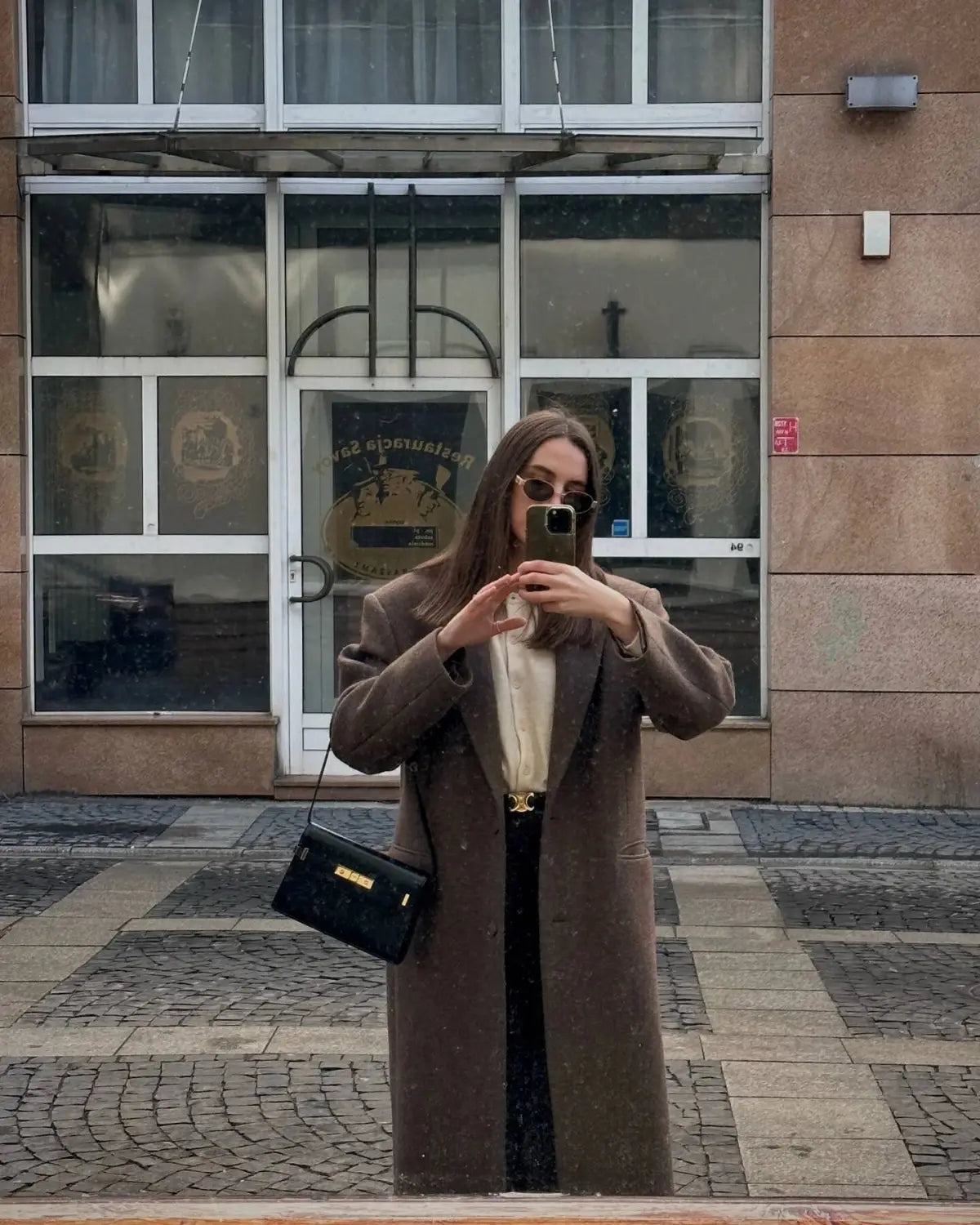 black crossbody bag with gold-tone hardware and minimalist design paired with brown wool blend overcoat for women winter commuter jacket.