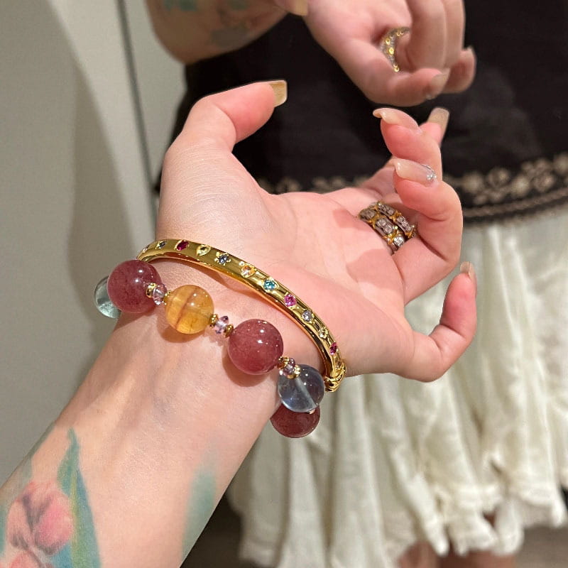 Ein Armreifarmband aus goldfarbenem Multigemsteinschmuck mit polierten, farbigen Edelsteinperlen und kleinen, eingearbeiteten Kristallen.