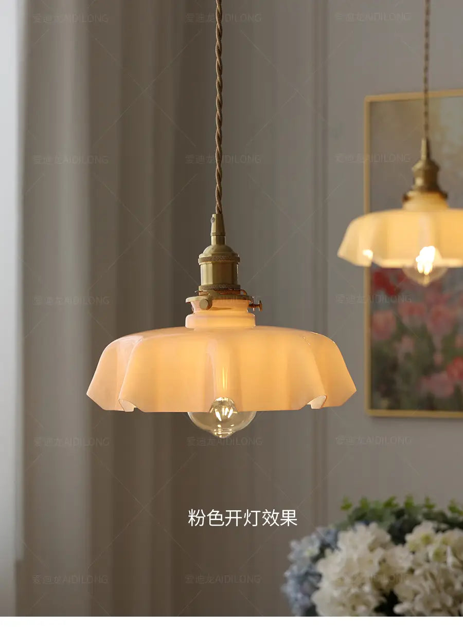 Un luminaire suspendu de teinte crème chaude à jupe florale en verre avec un abat-jour type pétale cannelé et une tête de lampe en cuivre visible depuis l’avant.