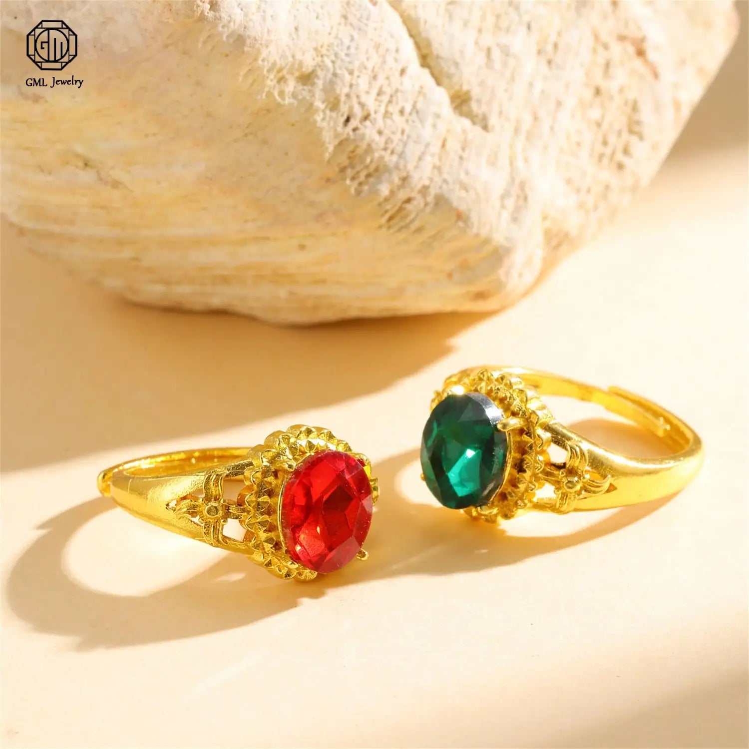 Two ornate sand gold adjustable rings featuring vibrant red oval and deep green emerald-cut gemstones set in fade resistant intricate filigree designs with matte wide bands.