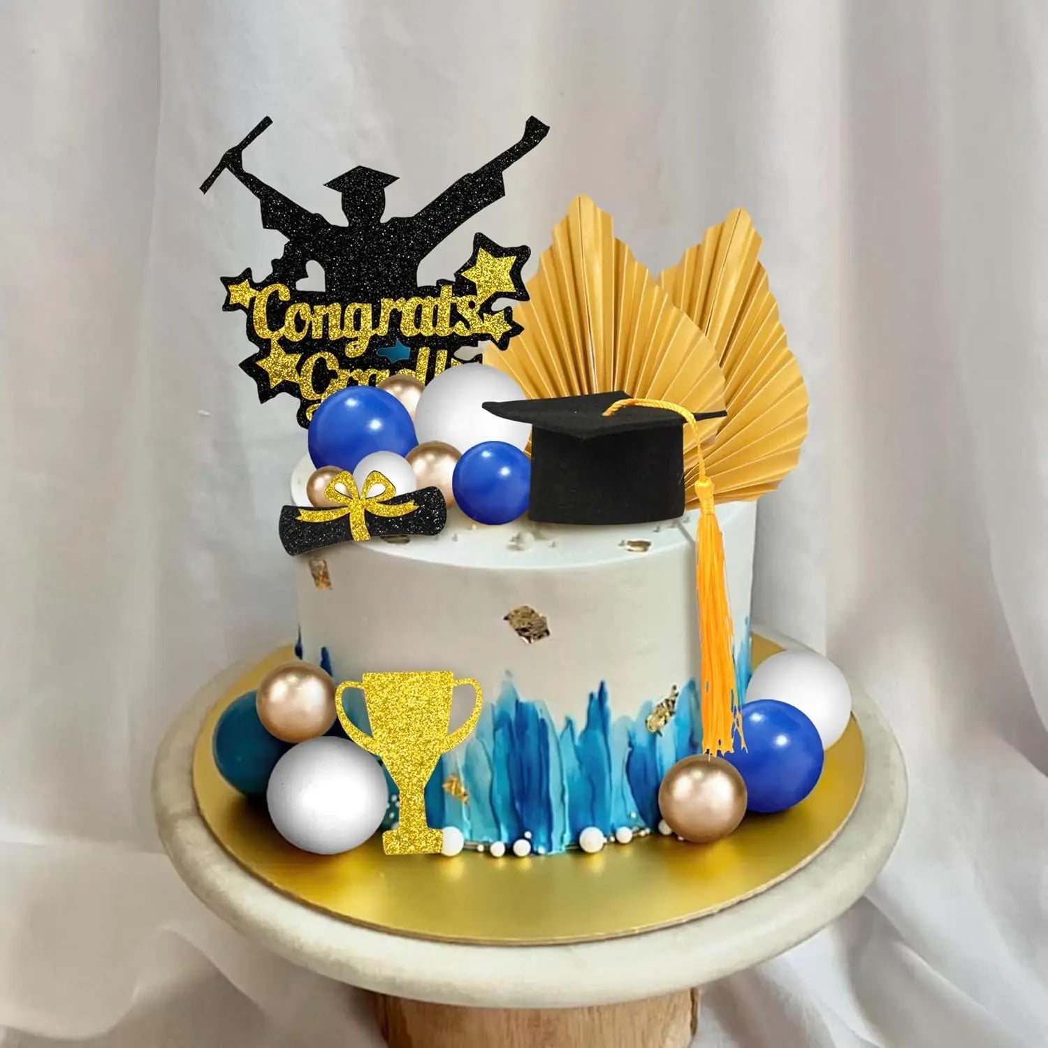 a white graduation cake with blue and gold accents featuring a black glittery topper of a graduate holding a diploma surrounded by navy silver and gold balloons graduation cake topper set for 2026 senior party