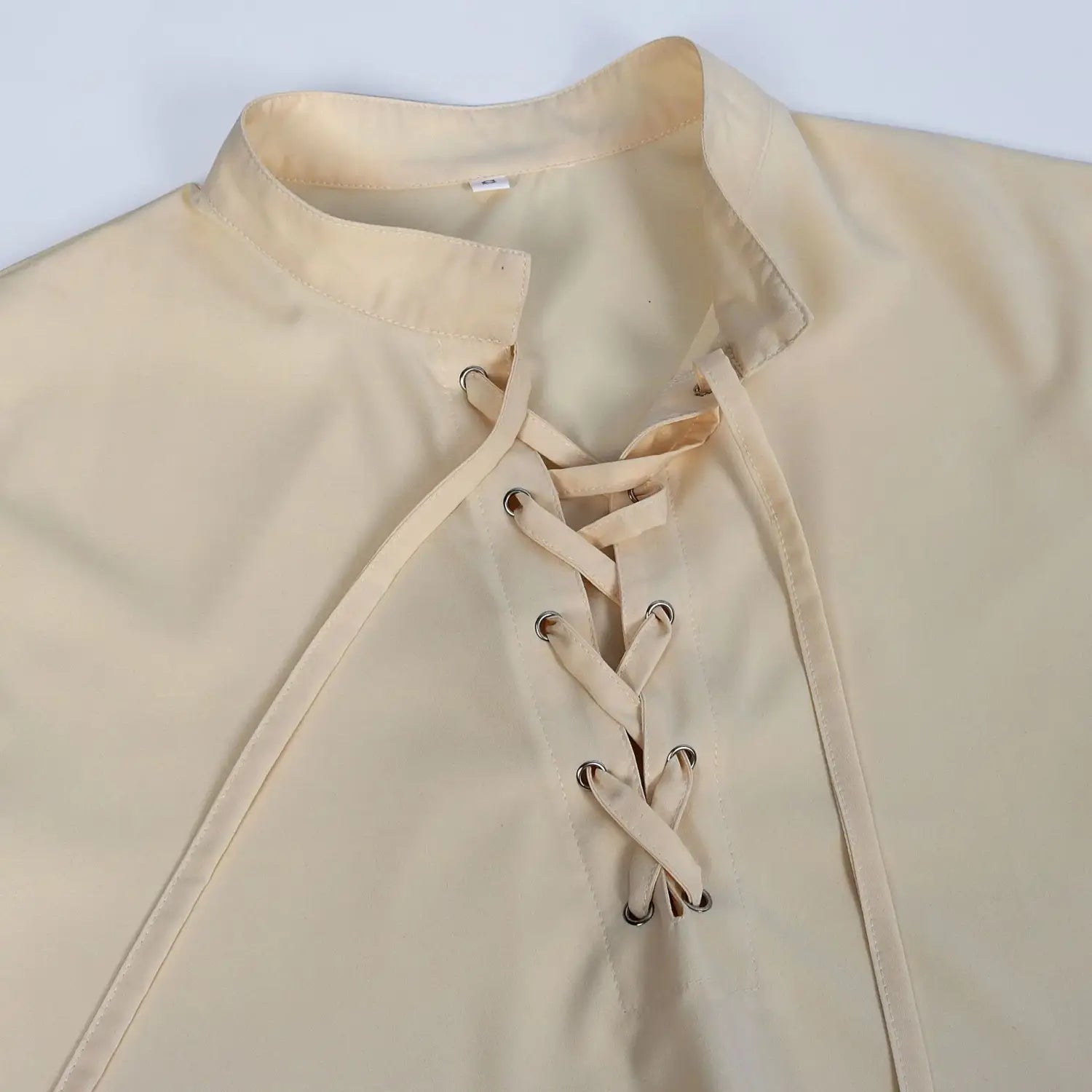Beige mens pirate medieval renaissance lace up shirt with stand collar and fabric ties threaded through metal eyelets shown from the front.