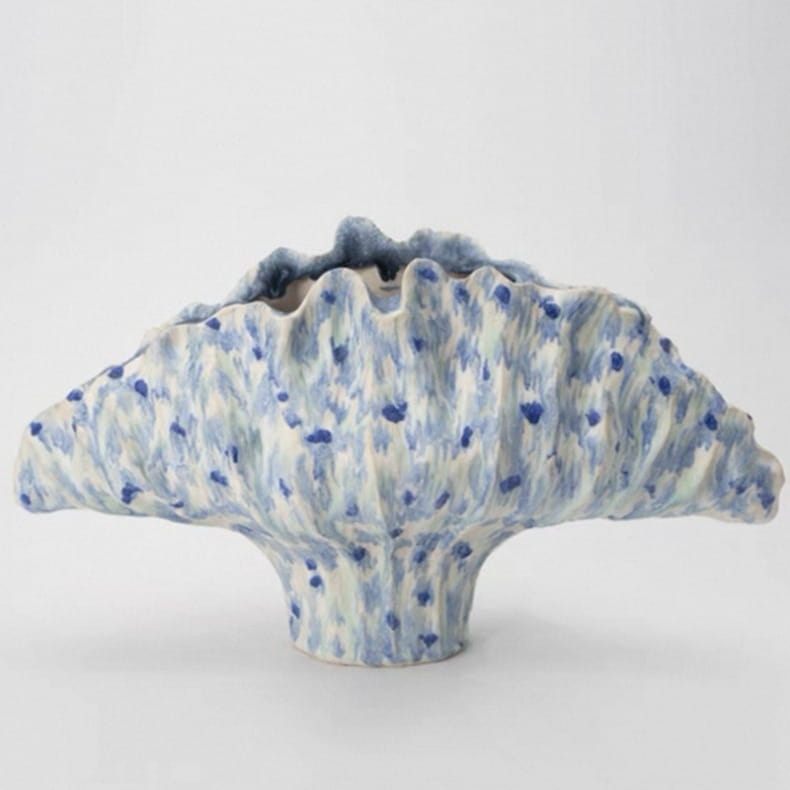 Un vase à fleurs en céramique avec un bord supérieur en forme d’éventail à motifs festonnés et un émail bleu moucheté sur une base en céramique blanc cassé mesurant 37 x 12 x 23 cm, conçu pour des effets décoratifs modernes de poterie et d’exposition.