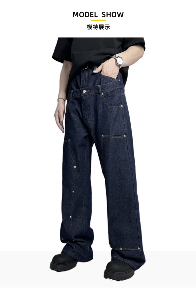 Jeans bruts en denim à jambe large à rivets pour hommes en indigo foncé, dotés de coutures renforcées et de rivets argentés le long des coutures latérales.