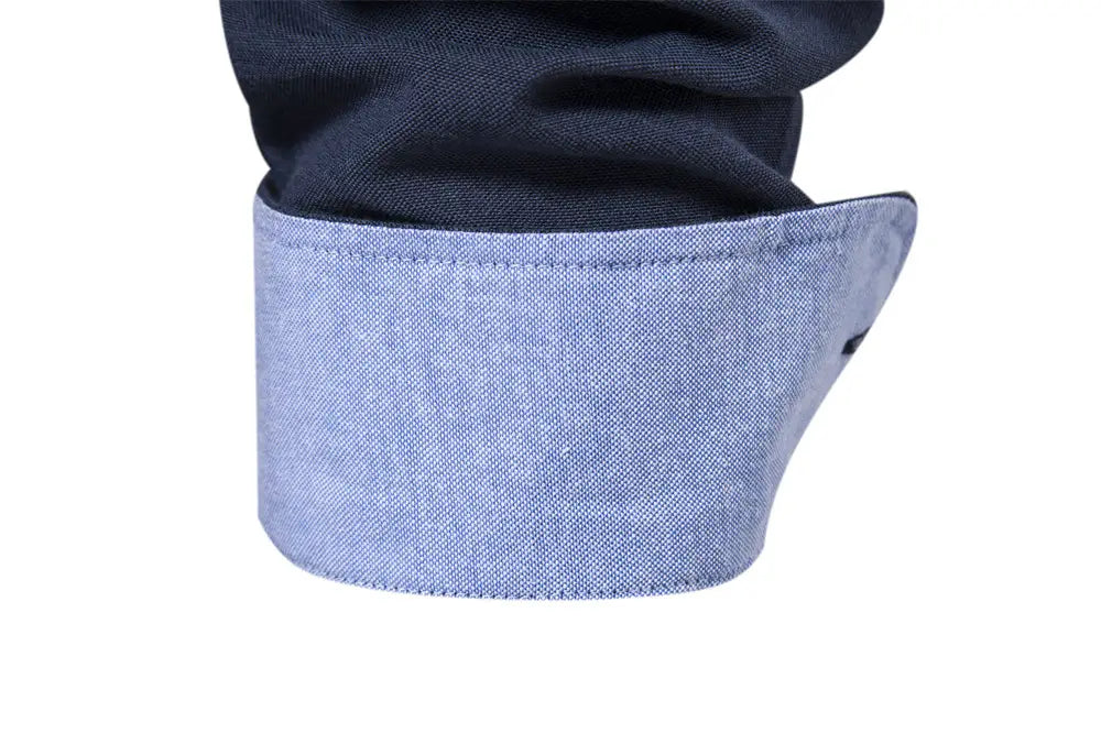 Light blue denim cuff with neatly stitched edges folded over a dark navy dress shirt sleeve showcasing fashion social shirts for men.