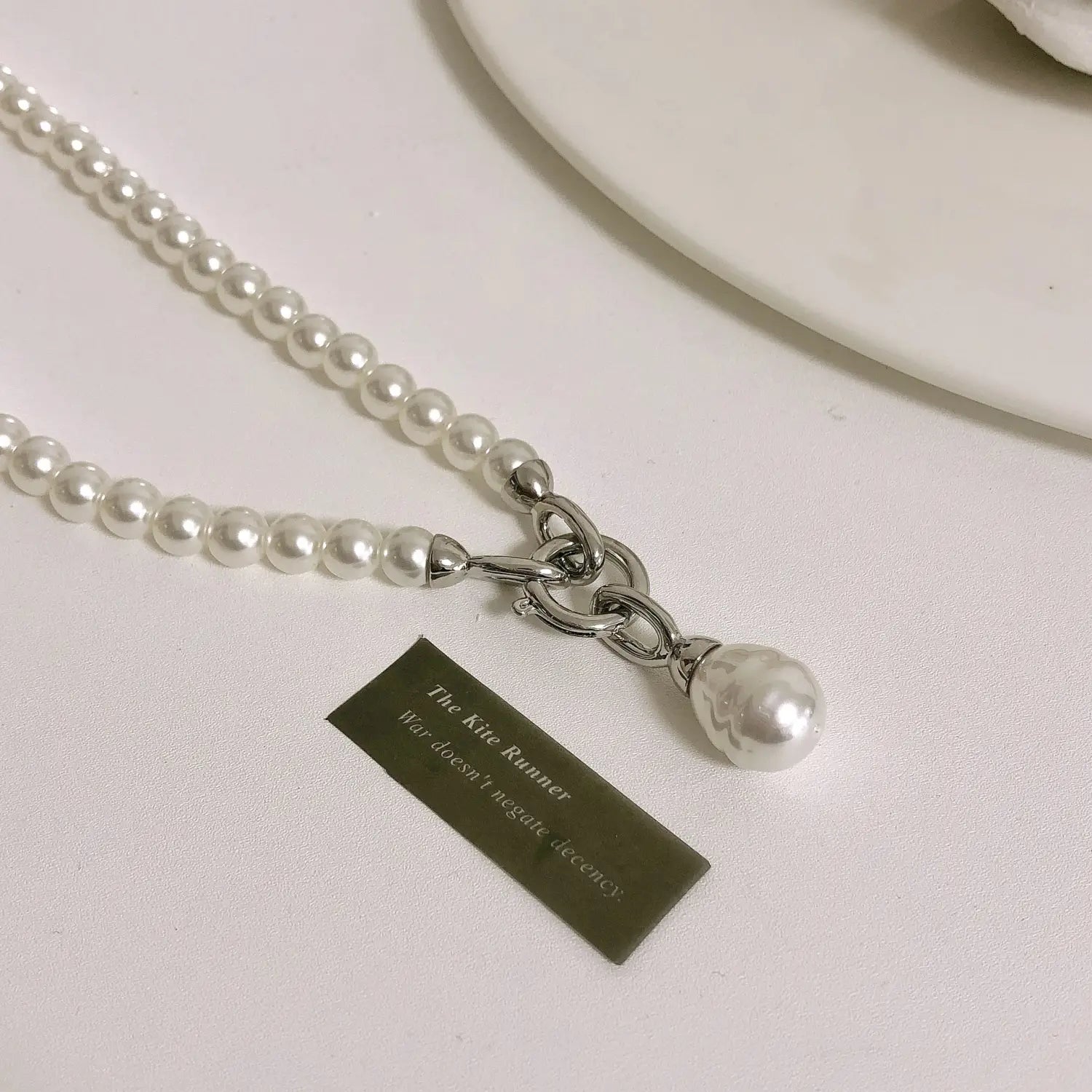 Un long collier délicat en perles en pendentif pour femmes, avec des perles blanches uniformes reliées par une chaîne argentée, et un pendentif en forme de goutte de perle suspendu avec élégance au centre.