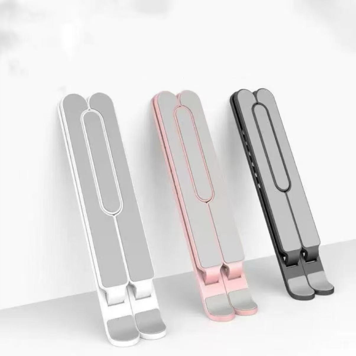 three slim foldable laptop stands in white pink and black showcasing their adjustable design for ergonomic use