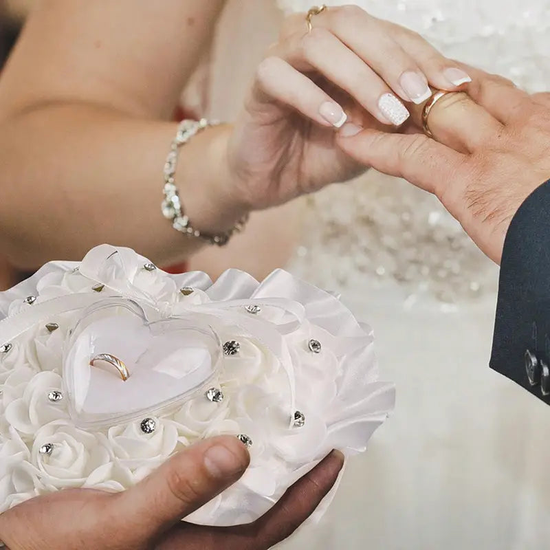 ハート型のクリアな収納部とシルバーのラインストーンのアクセントを備えた、白いフローラルのラインストーン結婚指輪リングピロー（ブライダルブーケ用）。