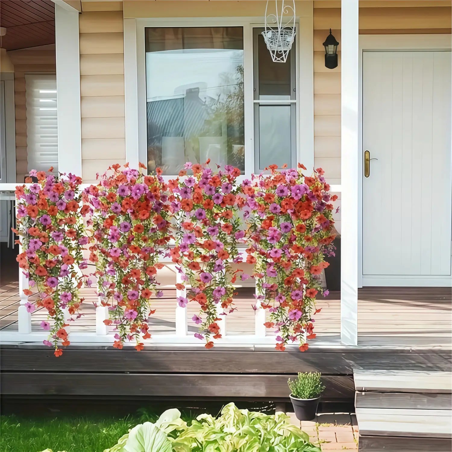 A vibrant cascade of artificial flowers in pink purple and orange resembling morning glory vines hangs as a flower bouquet from a white porch railing.