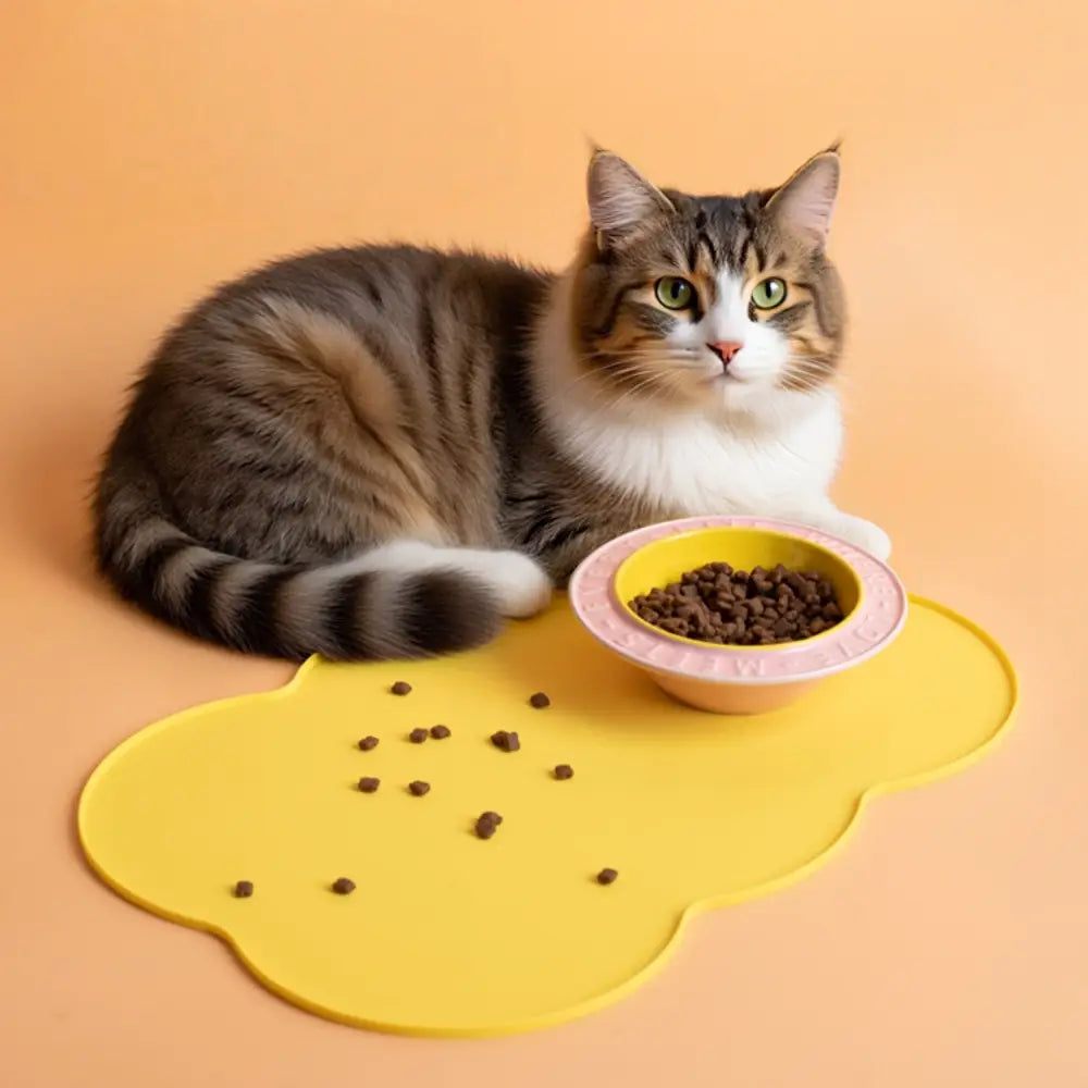 Alfombra de alimento para gatos de silicona amarilla con borde rosa y un cuenco a juego con alimento, diseñada para perros y gatos pequeños y medianos en la gama de alfombras de alimentación para mascotas de silicona con forma de nube.