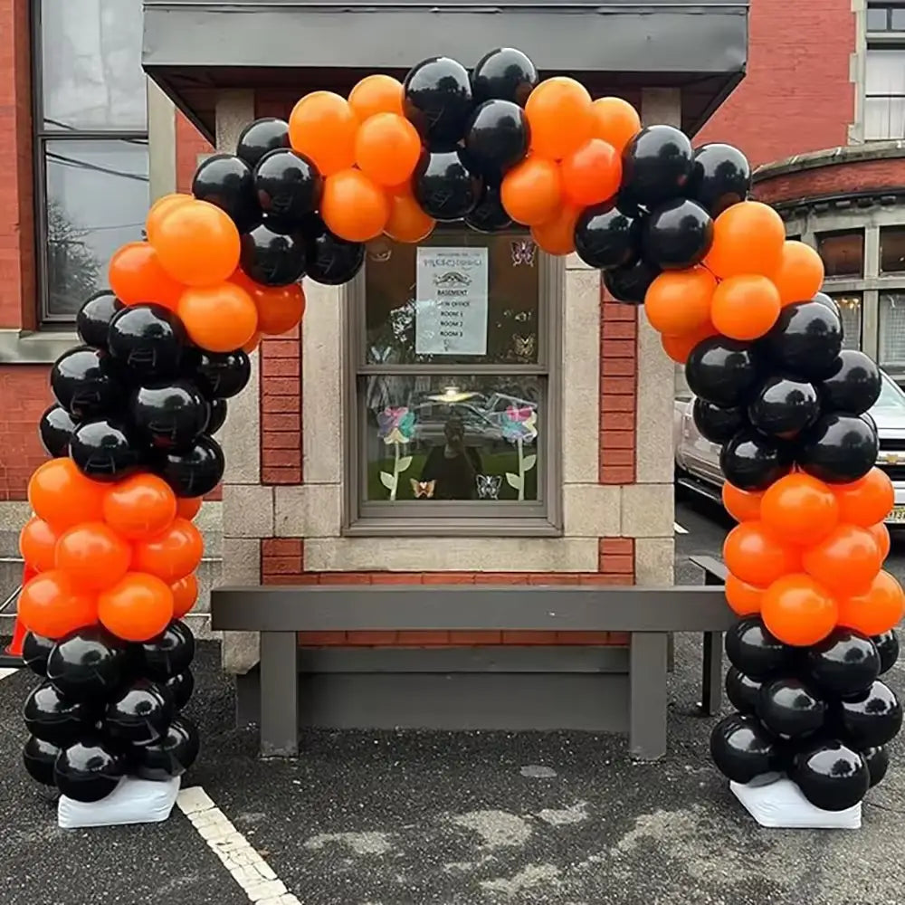 Ein schwarzes und goldenes Ballonbogen-Set für Partys mit einer festlichen schwarzen und orangefarbenen glänzenden Latexballon-Anordnung, die in abwechselnden Clustern eine dekorative Eingangsgestaltung bildet.