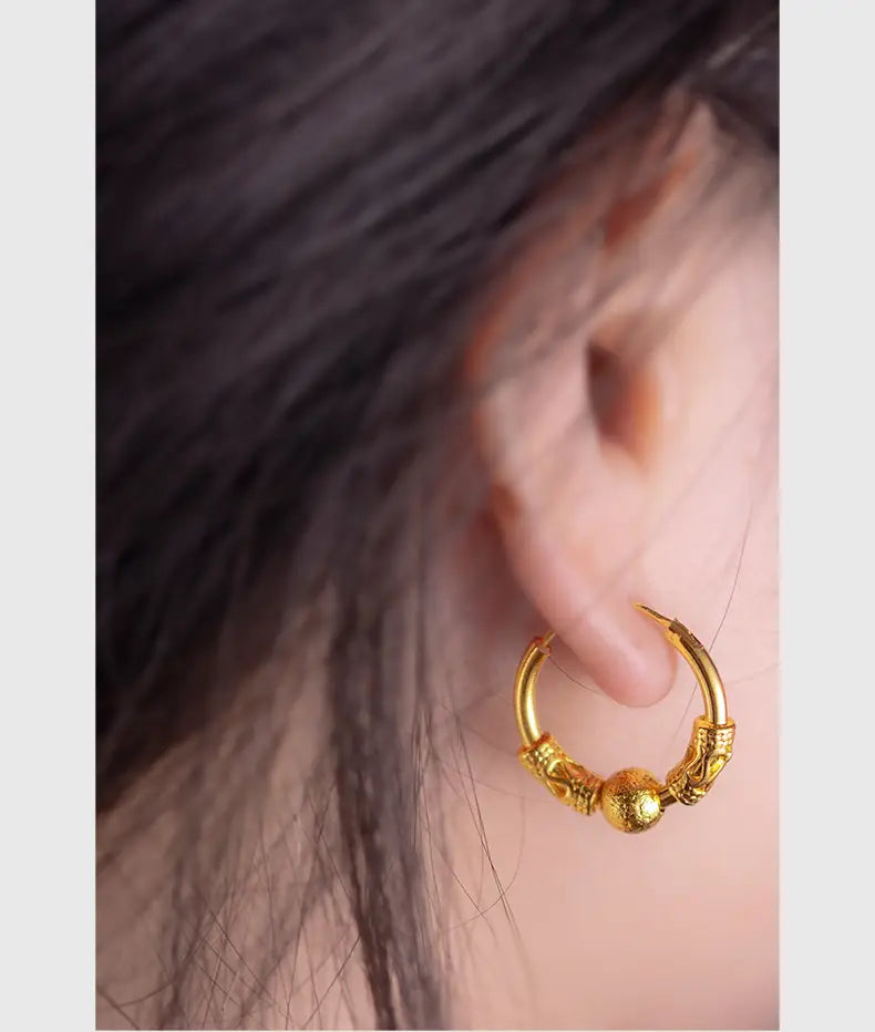 Ohrringe mit Gold-Drachenring mit einem goldenen Ringohrring und kunstvollen eingravierten Verzierungen sowie einer strukturierten kugelförmigen Perle, als feines Schmuck-Geschenk.