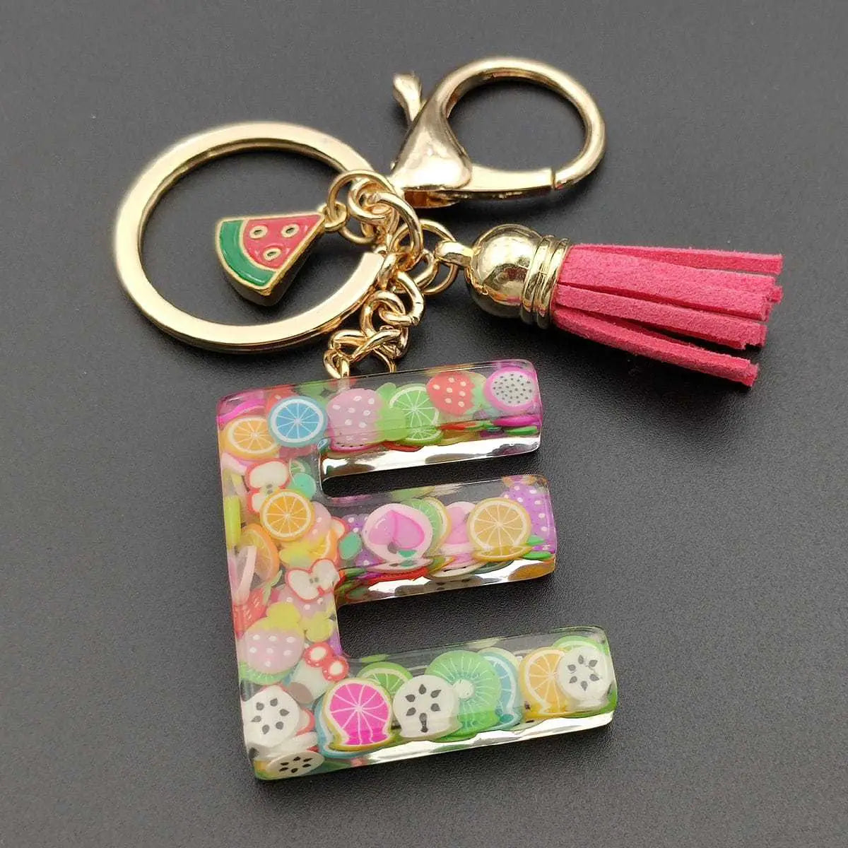 A vibrant transparent resin keychain shaped like the letter e with colorful fruit slices embedded and decorated with a gold-tone clasp and pink tassel for the fruit letter resin keychain initial alphabet key ring.