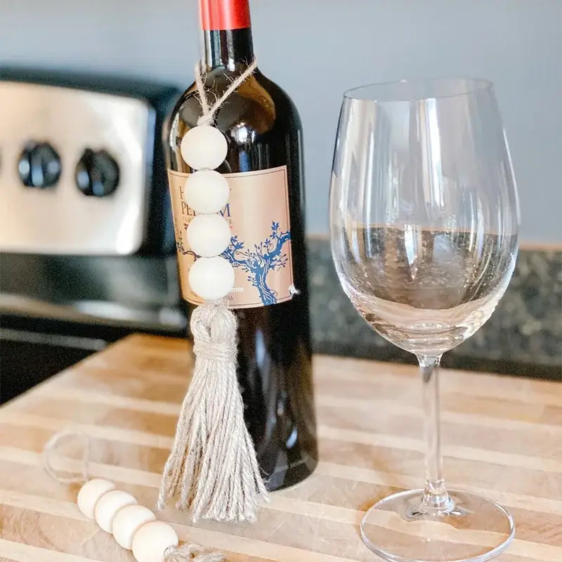 Eine dunkle Glasflasche für Wein, verziert mit einem weißen hölzernen Perlengirlanden-Tassel-Anhänger.