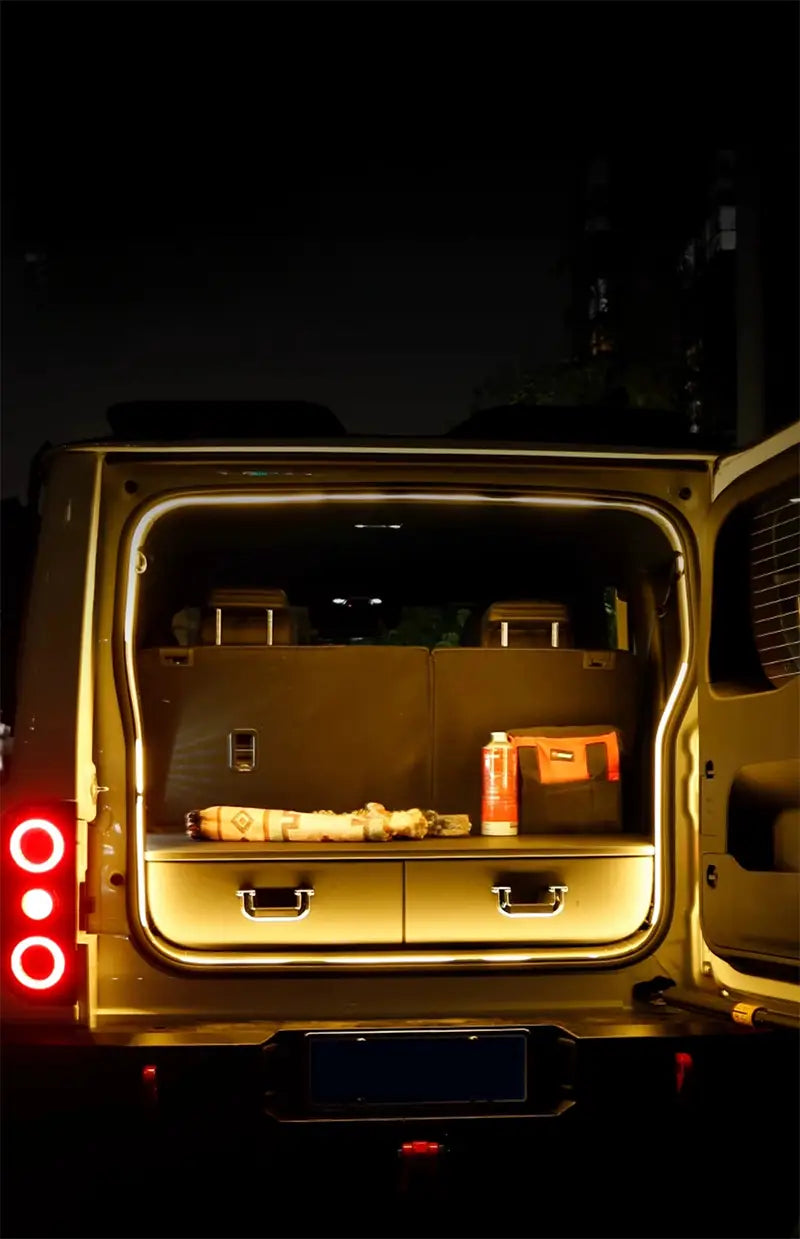 The illuminated rear cargo area of a gold-colored suv showcases two sleek metallic-finished drawers with minimalist handles featuring car trunk lighting fit for modified auto trunk use.