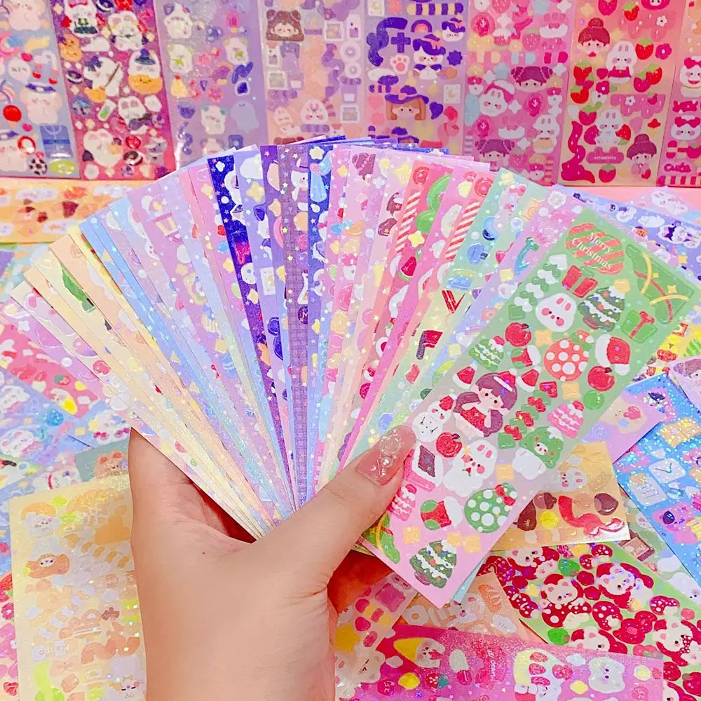 Eine Hand hält einen Fächer mit farbenfrohen, glitzernden kawaii-hübschen Cartoon-Aufklebern mit festlichen Motiven für Scrapbooking- und Tagebuchdekoration.
