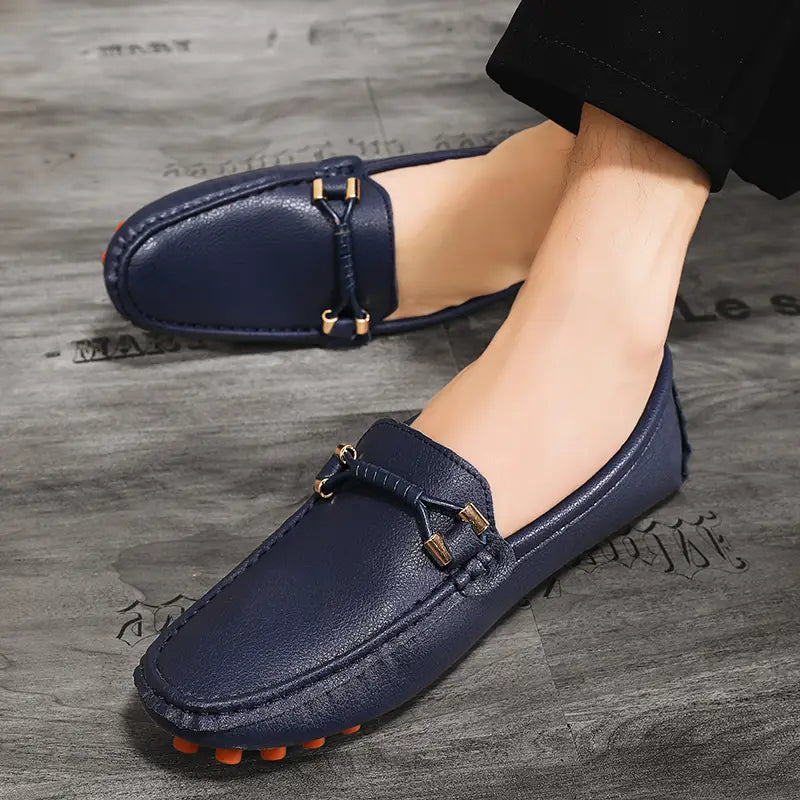 Chaussures à enfiler habillées en cuir bleu marine pour hommes, avec des accents métalliques ton or et des semelles en caoutchouc orange pour un port décontracté sans effort.