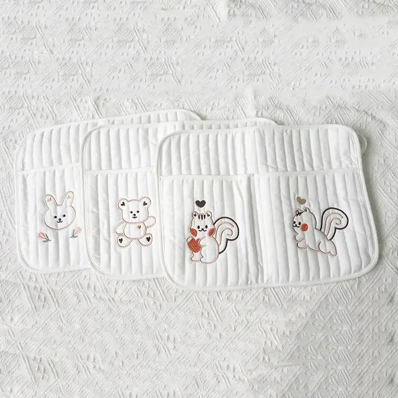 クマの刺繍が施された白いキルティング製ベビーカー用オーガナイザー袋で、ウサギ、クマ、リスがどんぐりとハートを抱えた刺繍のカートゥーン動物が施されています。