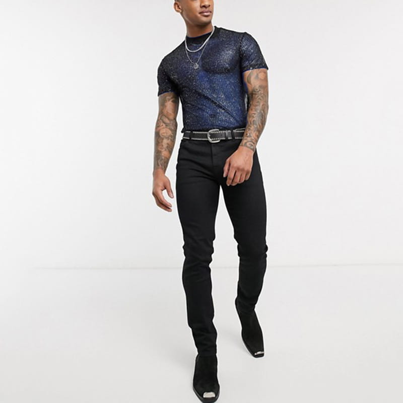 A man wearing a dark blue men glitter mesh t-shirt with a see-through textured pattern and black slim-fit jeans.