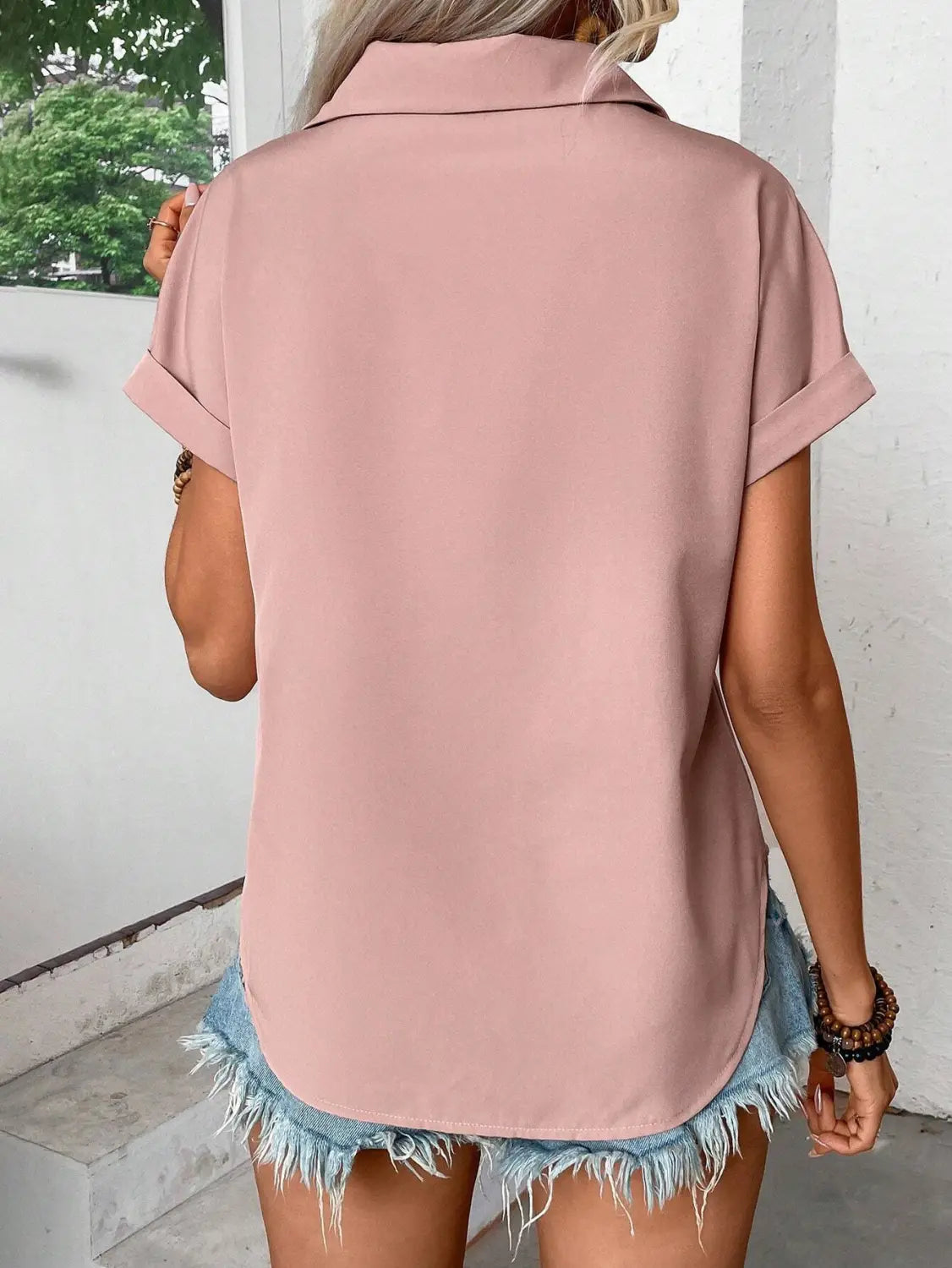 A soft pink short sleeve button up blouse for women with a relaxed fit and rolled cuffs highlighting the sleeve length.