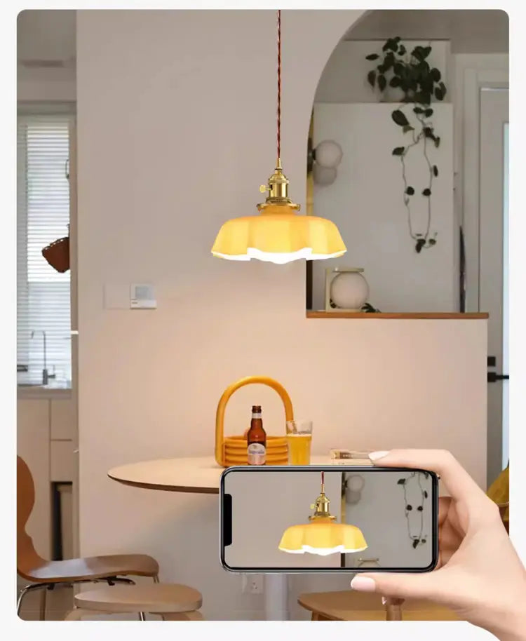 Luminaire suspendu à jupe florale en verre jaune à bords ondulés avec tête de lampe en cuivre et quincaillerie en laiton, vu depuis un angle avant.